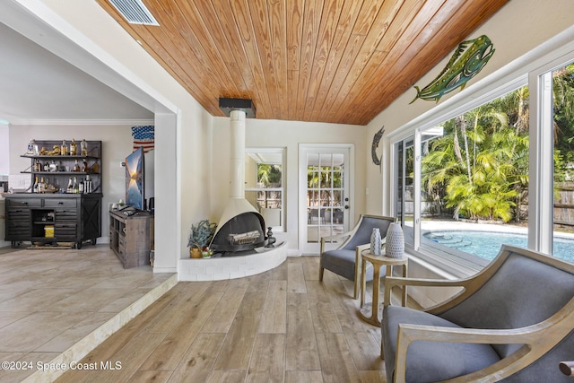 living area featuring wood ceiling, wood-type flooring, a wood stove, and plenty of natural light