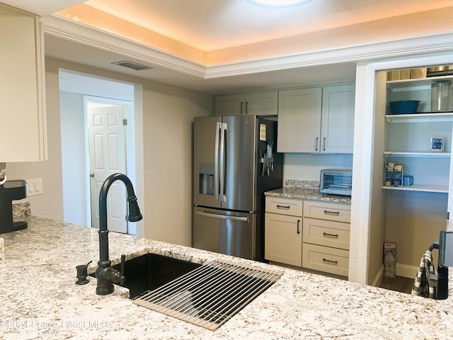 kitchen with a sink, stainless steel fridge with ice dispenser, light stone counters, and visible vents