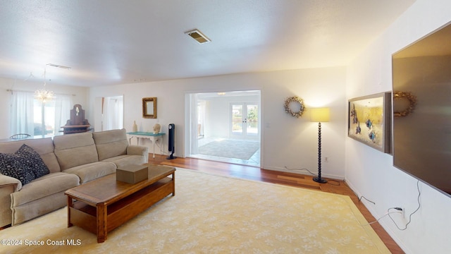 living room featuring light hardwood / wood-style flooring, french doors, and a notable chandelier