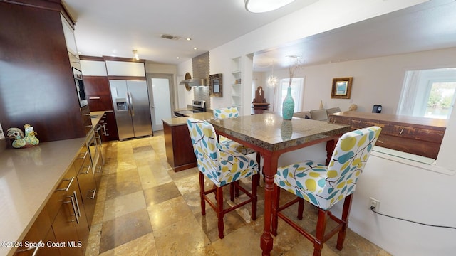 kitchen with wall chimney exhaust hood, a kitchen breakfast bar, built in features, built in refrigerator, and a kitchen island