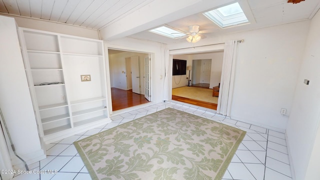 tiled spare room featuring beamed ceiling, ceiling fan, built in shelves, and a skylight