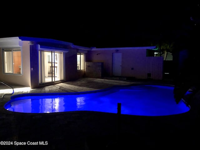 pool at night featuring a patio