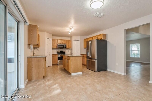 kitchen with stainless steel appliances, a textured ceiling, sink, and a kitchen island with sink