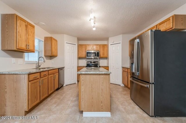 kitchen with appliances with stainless steel finishes, a textured ceiling, a kitchen island with sink, light stone countertops, and sink