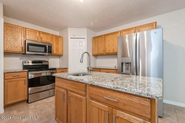 kitchen with sink, light tile patterned flooring, a textured ceiling, stainless steel appliances, and a kitchen island with sink