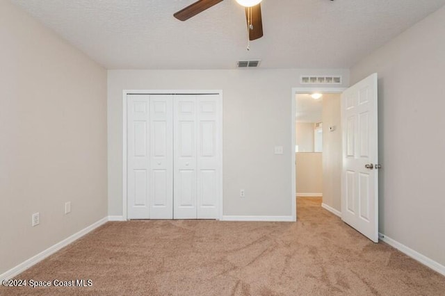 unfurnished bedroom featuring a closet, ceiling fan, a textured ceiling, and light colored carpet