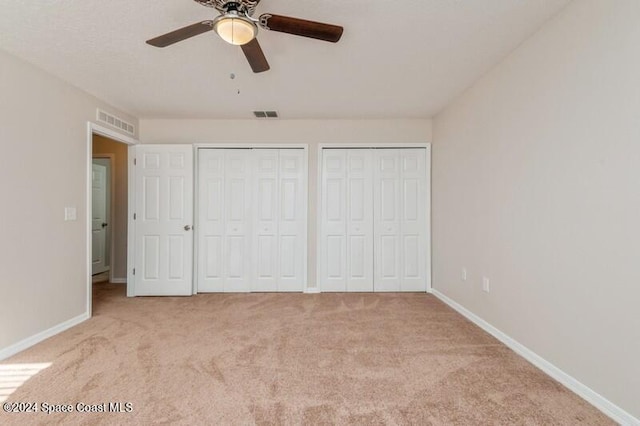 unfurnished bedroom featuring light carpet, two closets, and ceiling fan