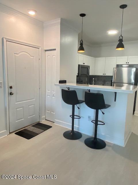 kitchen with white cabinetry, stainless steel appliances, decorative light fixtures, a kitchen bar, and decorative backsplash