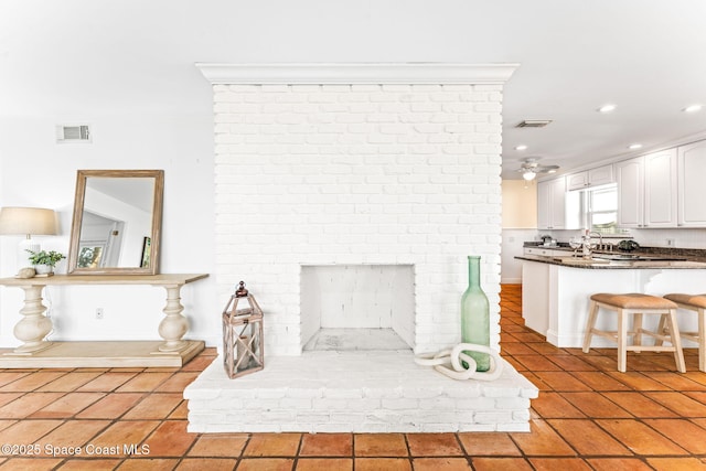 unfurnished living room featuring a brick fireplace, sink, light tile patterned floors, and ceiling fan