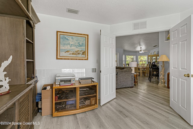 home office with ceiling fan, light hardwood / wood-style floors, and a textured ceiling