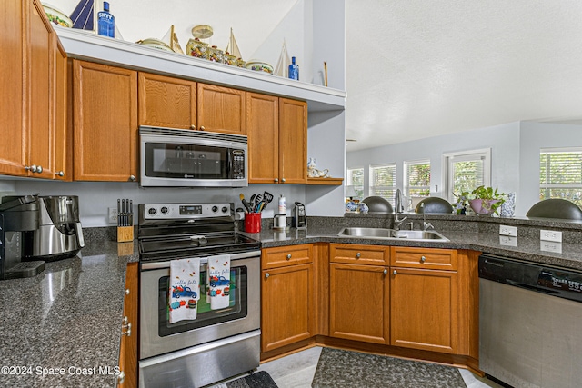 kitchen featuring appliances with stainless steel finishes, dark stone counters, and sink