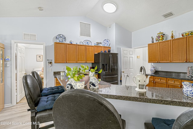 kitchen featuring kitchen peninsula, stainless steel fridge, light hardwood / wood-style flooring, dark stone countertops, and lofted ceiling