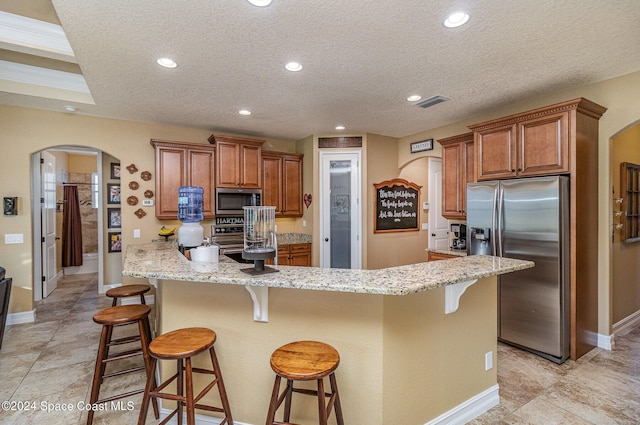 kitchen with a breakfast bar area, stainless steel appliances, a center island, light stone counters, and a textured ceiling