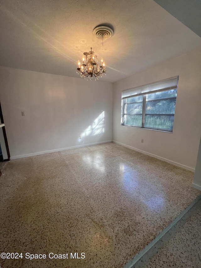 empty room featuring a notable chandelier and a textured ceiling