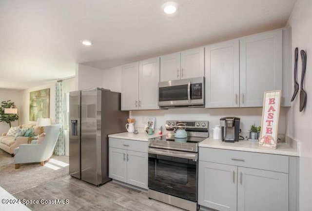 kitchen featuring open floor plan, light wood-style flooring, stainless steel appliances, light countertops, and gray cabinetry