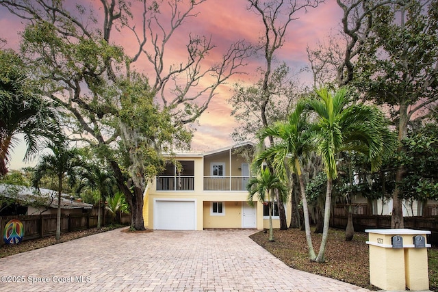 beach home with driveway, fence, a balcony, and stucco siding