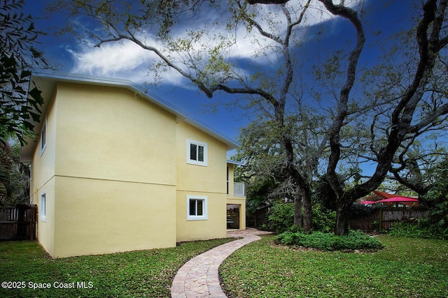 view of side of home with a lawn, fence, and stucco siding