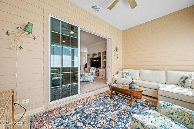 living room with wood walls, hardwood / wood-style flooring, and ceiling fan