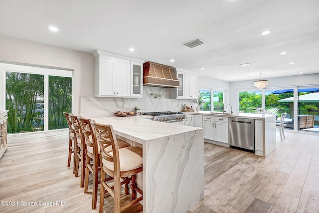 kitchen with pendant lighting, premium range hood, appliances with stainless steel finishes, light hardwood / wood-style floors, and white cabinetry