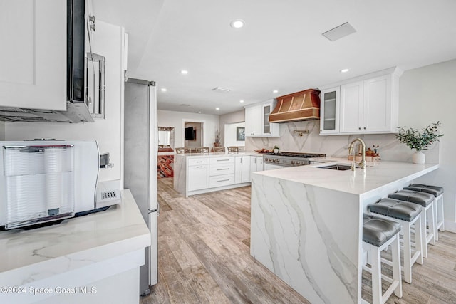 kitchen featuring sink, kitchen peninsula, light wood-type flooring, custom range hood, and white cabinetry