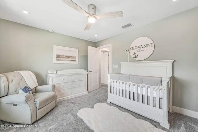 bedroom with ceiling fan, light colored carpet, and a crib