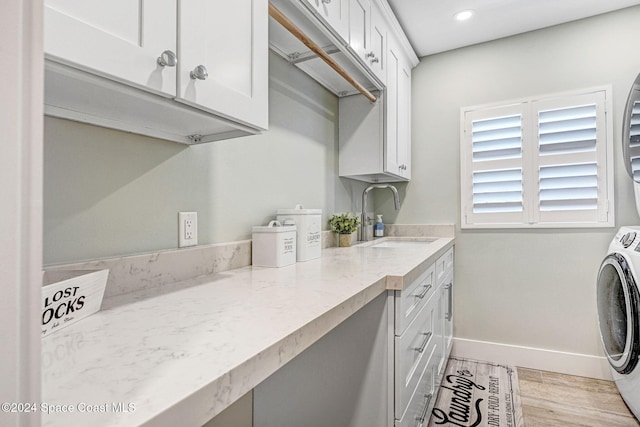 clothes washing area featuring washer / clothes dryer, sink, cabinets, and light hardwood / wood-style floors