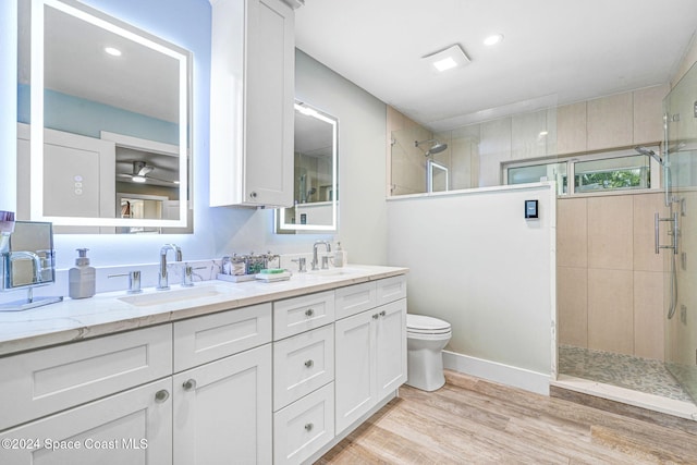 bathroom featuring toilet, vanity, wood-type flooring, and tiled shower