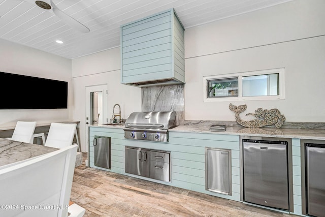 kitchen with stainless steel fridge, light wood-type flooring, light stone counters, and sink