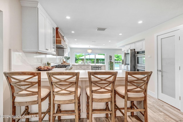 kitchen featuring white cabinetry, stainless steel appliances, kitchen peninsula, light hardwood / wood-style floors, and a breakfast bar area