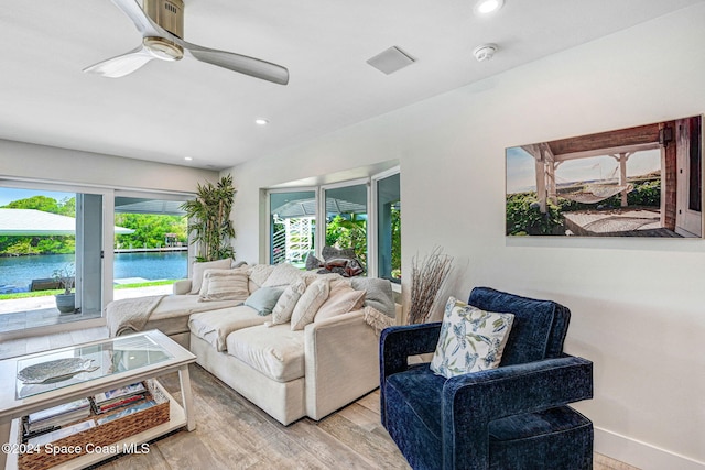 living room featuring ceiling fan, light hardwood / wood-style flooring, and a water view