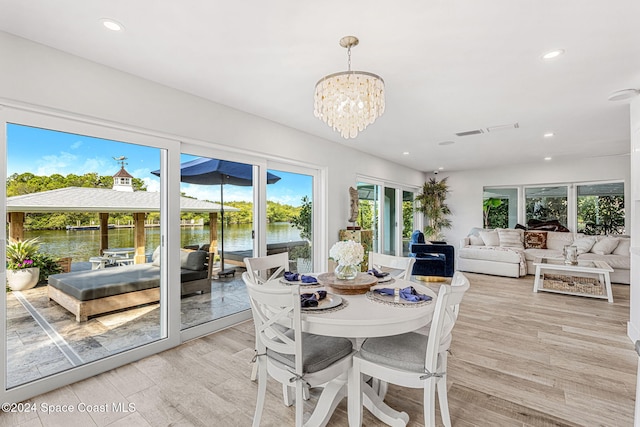 dining area with a notable chandelier, a water view, and light wood-type flooring