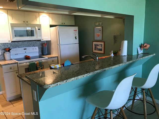 kitchen featuring white appliances, backsplash, white cabinets, dark stone countertops, and a kitchen bar