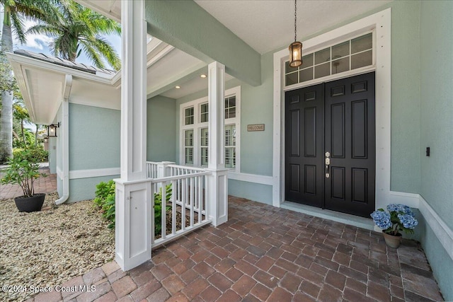 view of exterior entry featuring a porch and stucco siding