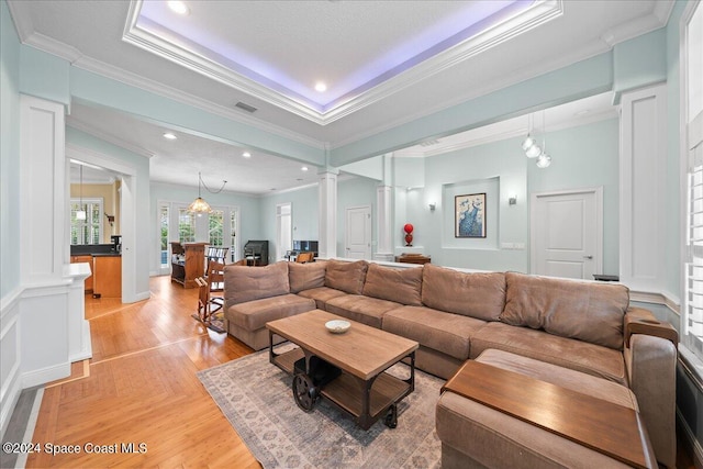 living room with decorative columns, an inviting chandelier, a tray ceiling, and ornamental molding