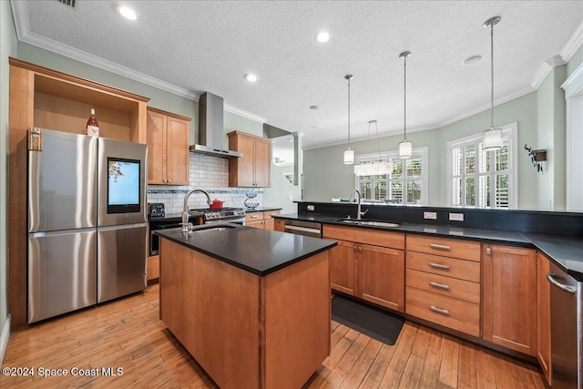 kitchen with pendant lighting, stainless steel appliances, wall chimney range hood, and light wood-type flooring