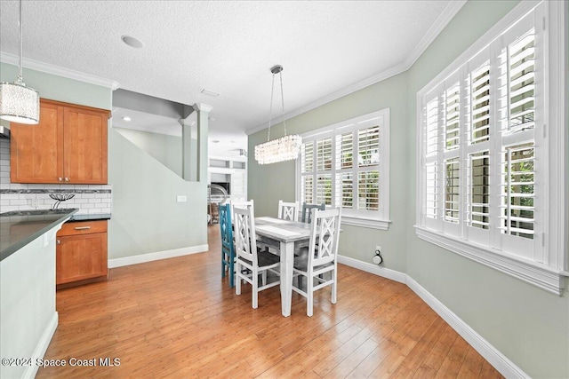 dining room featuring an inviting chandelier, light hardwood / wood-style flooring, crown molding, a textured ceiling, and a fireplace