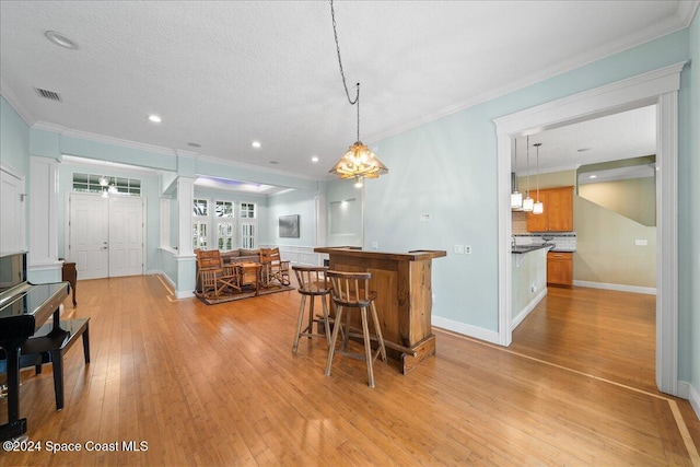 kitchen featuring light wood-type flooring, a kitchen breakfast bar, a textured ceiling, and crown molding