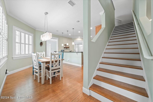 dining room with crown molding, light wood-type flooring, a textured ceiling, and an inviting chandelier