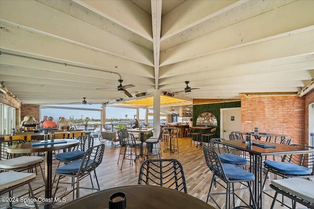 dining space with wood-type flooring, vaulted ceiling, ceiling fan, and brick wall