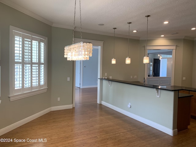 kitchen with an inviting chandelier, hardwood / wood-style floors, pendant lighting, a textured ceiling, and ornamental molding