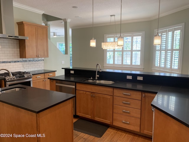 kitchen featuring appliances with stainless steel finishes, crown molding, wall chimney range hood, a center island with sink, and light hardwood / wood-style floors