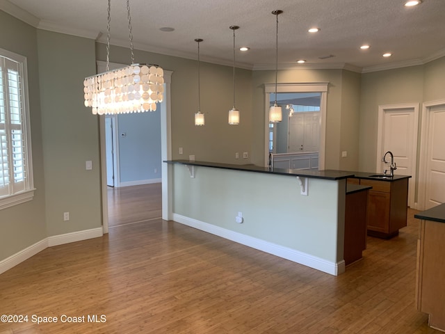 kitchen featuring a textured ceiling, crown molding, sink, decorative light fixtures, and hardwood / wood-style flooring