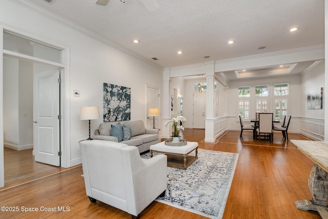 living room with wainscoting, ornamental molding, wood finished floors, a textured ceiling, and ornate columns