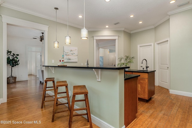 kitchen with visible vents, brown cabinetry, a breakfast bar, decorative light fixtures, and a sink