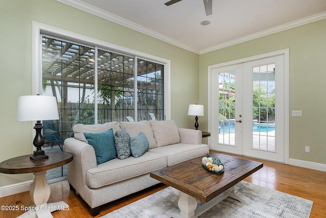 living area featuring wood finished floors, a ceiling fan, baseboards, ornamental molding, and french doors