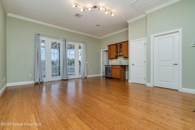 unfurnished living room featuring visible vents, baseboards, light wood-style flooring, wine cooler, and crown molding