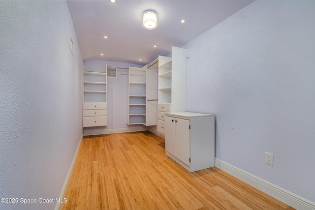 spacious closet with light wood-style floors, lofted ceiling, and visible vents