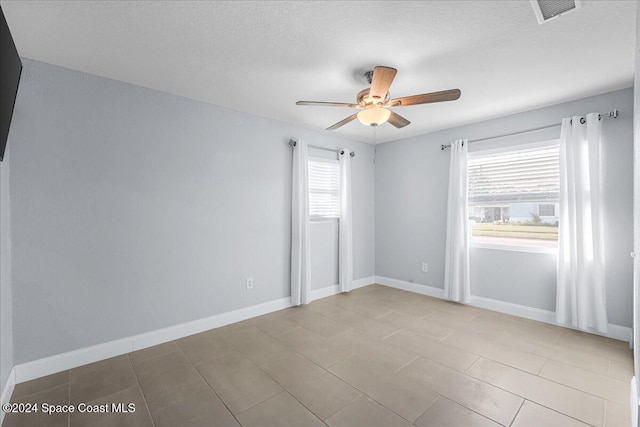 empty room with a wealth of natural light, a textured ceiling, and ceiling fan