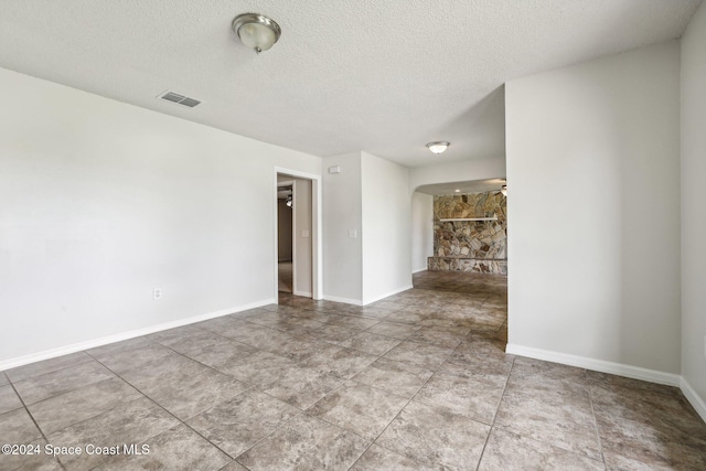 unfurnished living room with a textured ceiling, arched walkways, and baseboards