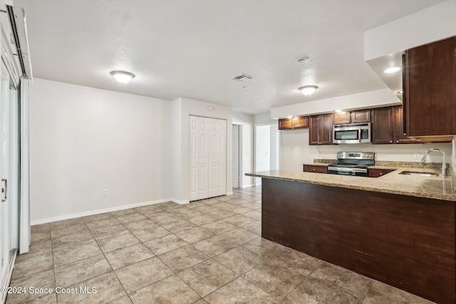 kitchen featuring stainless steel appliances, a sink, light stone counters, dark brown cabinets, and light tile patterned floors